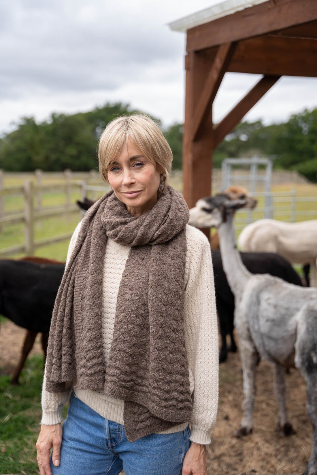 model wearing an alpaca wrap with alpacas in the background